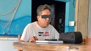 Hombre sentado en una mesa de madera y con los ojos tapados.