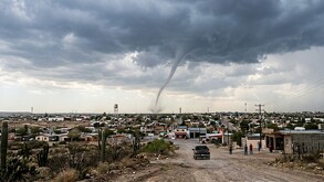 Se observa la formación de un tornado, se ve una camioenta y varias casas.