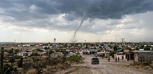 Se observa la formación de un tornado, se ve una camioenta y varias casas.