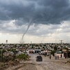 Se observa la formación de un tornado, se ve una camioenta y varias casas.