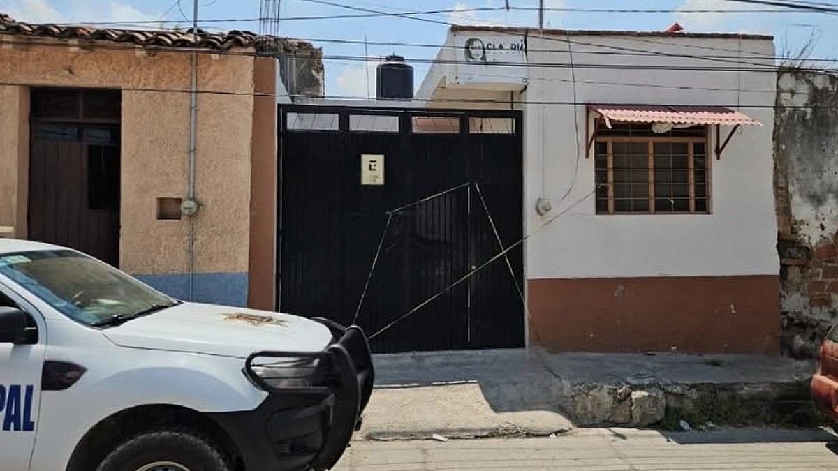 Exterior de una casa con portón negro acordonada por una cinta policiaca amarilla y una patrilla de la Policía de Zapotiltic estacionada enfrente