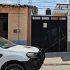 Exterior de una casa con portón negro acordonada por una cinta policiaca amarilla y una patrilla de la Policía de Zapotiltic estacionada enfrente