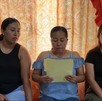 una mujer lee un documento mientras otras dos mujeres la acompañan