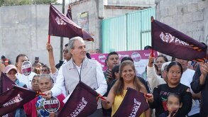 Mandatario entre ciudadanas de Puebla con banderas del partido morena a un lado de la calle pavimentada