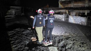 Dos elementos de SINAPROC parados sobre unas rocas y siendo alumbrados con una lámpara en el exterior de una vivienda donde brotó un géiser