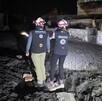 Dos elementos de SINAPROC parados sobre unas rocas y siendo alumbrados con una lámpara en el exterior de una vivienda donde brotó un géiser