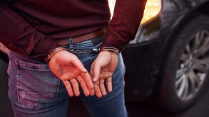 Hombre visto de la cintura hacia abajo con las manos en la espalda y esposas colocadas durante un arresto delante de un automóvil negro