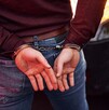 Hombre visto de la cintura hacia abajo con las manos en la espalda y esposas colocadas durante un arresto delante de un automóvil negro