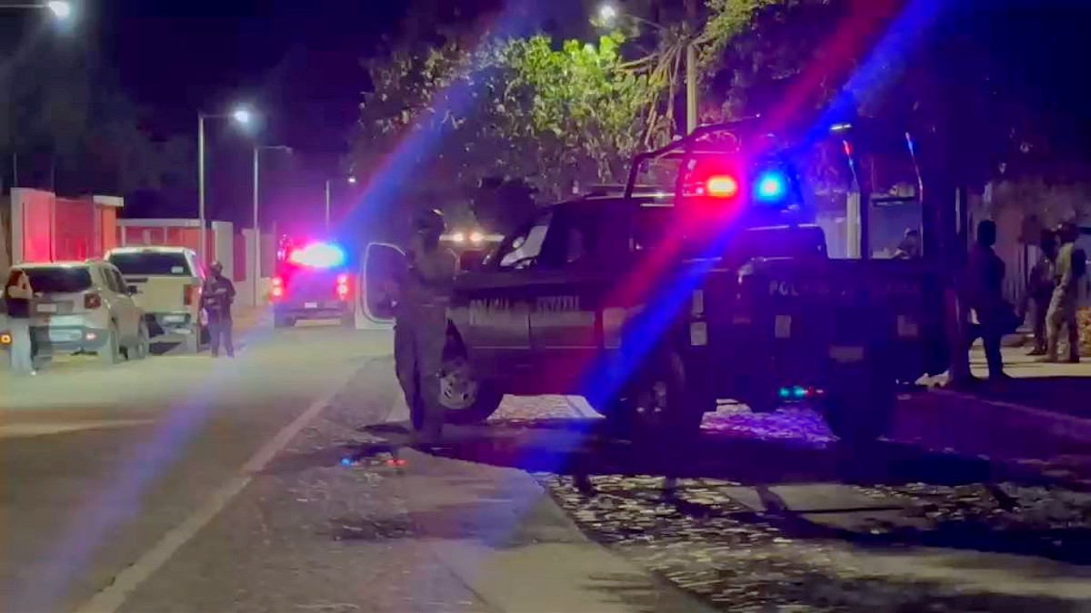 Patrulla de la Policía del Estado de Colima con la sirena encendida y militares alrededor en medio de una calle con personas y autos estacionados