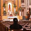 Persona reza adentro de una iglesia rodeada de santos