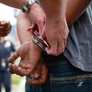 Adolescente con las manos en la espalda siendo esposado por tres policías durante un arresto al costado de un automóvil
