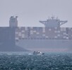 Un barco portacontenedores se ve fondeado mientras una lancha pasa por delante en el estrecho de Ormuz, cerca de Bandar Abbas, Irán, el sábado 2 de mayo de 2026