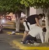 Un hombre agarrando por el cuello de la camisa a otro que se encuentra en el suelo de la jardinera de un estacionamiento