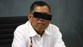 Foto de archivo de Gerardo Mérida Sánchez sentado en una silla negra con un gesto en el rostro, portando una camisa blanca y lentes.