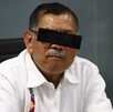 Foto de archivo de Gerardo Mérida Sánchez sentado en una silla negra con un gesto en el rostro, portando una camisa blanca y lentes.