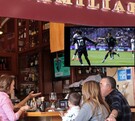 Restaurante con partido de México vs Ghana en la pantalla y hombres conviviendo