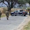 Dos militares del Ejército Mexicano caminando hacia una patrulla de la Policía de Zapopan delante de un área acordonada con un cuerpo cubierto sobre la calle