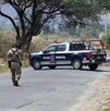 Dos militares del Ejército Mexicano caminando hacia una patrulla de la Policía de Zapopan delante de un área acordonada con un cuerpo cubierto sobre la calle