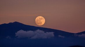 La luna llena sobre el horizonte y una montaña