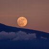 La luna llena sobre el horizonte y una montaña