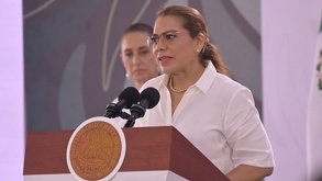 Mujer de lentes hablando ante una tribuna.