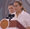 Mujer de lentes hablando ante una tribuna.