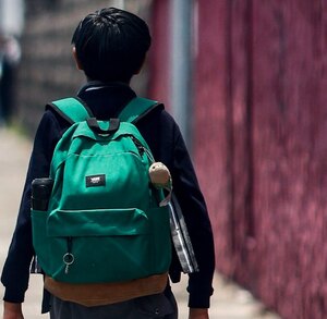 Niño con una mochila caminando hacia una escuela.