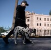 Se ve a un hombre caminando, usa lentes de sol y lleva con una correa a un perro dalmata.