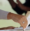 Imagen en primer plano de una mano colocando una boleta electoral dentro de una urna. El fondo es desenfocado.