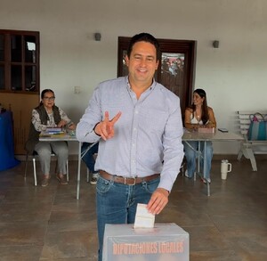 Se observa a un hombre metiendo un papel a una urna y hay al fondo otras mujeres.