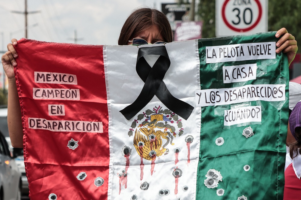 Mujer sostiene una bandera de México con consignas de protesta.