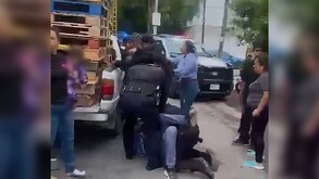 Oficiales de la Policía de Zapopan sometiendo a un joven motociclista al lado de una camioneta con tarimas de madera y personas alrededor