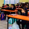 Se observa a varios alumnos en sus pupitres dentro de un salón de clases.