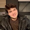 Influencer Jair Sánchez sentado delante de ventanas en un departamento mientras mira hacia un costado