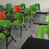 Mesabancos escolares con sillas color verde y naranjas dentro de un salón de clases vacío por suspensión de clases