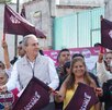 Mandatario entre ciudadanas de Puebla con banderas del partido morena a un lado de la calle pavimentada