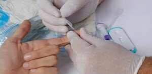Mano de un persona con el dedo extendido realizándose una prueba de ITS con la extracción de una muestra de sangre con guantes médicos alrededor
