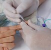 Mano de un persona con el dedo extendido realizándose una prueba de ITS con la extracción de una muestra de sangre con guantes médicos alrededor