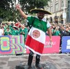 Hombre vistiendo un poncho con la bandera de México y un sombrero de charro delante de la barda y el público del Fan Festival en Guadalajara