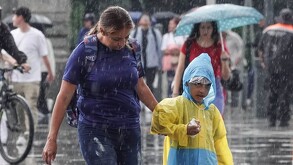 Se observa a una señora y un niño, está lloviendo y el niño se protege del agua con un paraguas.