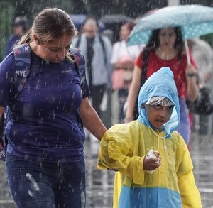 Se observa a una señora y un niño, está lloviendo y el niño se protege del agua con un paraguas.