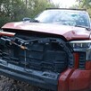 Camioneta color rojo con la fascia desbaratada, el cristal frontal roto con múltiples balazos y las puertas abiertas y dañadas en medio de terreno con árboles