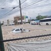 Se observa una inundación y un carro color gris en medio de la corriente de agua.