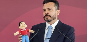 Hombre vestido de traje sosteniendo un peluche colorido.