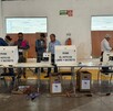 Se observa a varias personas de pie y tienen unas urnas de votar adelante.