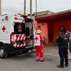 Se observa una ambulancia en color rojo y balnco y unas personas en medio de la calle.