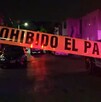 Se observa una cinta amarilla de precaución, es de noche y hay una patrulla.