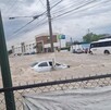 Se observa una inundación y un carro color gris en medio de la corriente de agua.