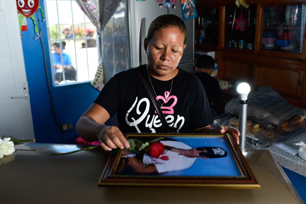 Mujer junto a un féretro que carga la foto de un fallecido.