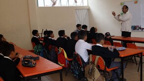Se observa a varios niños sentados en pupitres en un salón de clases.